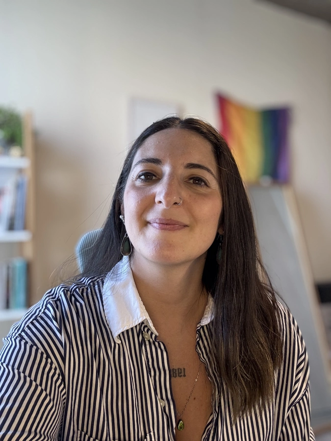 Retrato de Emilia Alegre sonriendo, con una bandera del orgullo de fondo